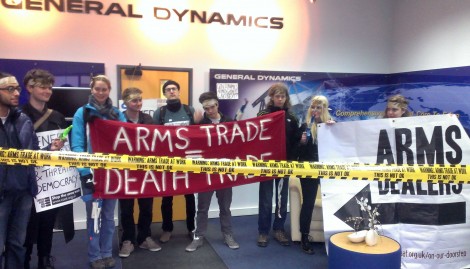 Students stand inside General Dynamics with "arms trade equals death trade" banner