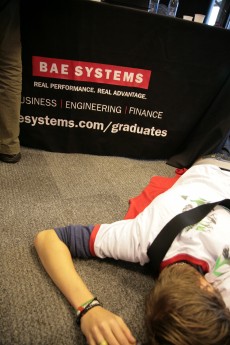 Student lying down as if dead in front of a BAE Systems stall