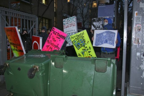 Masked protesters stand behind giant cardboard books and upturned bins